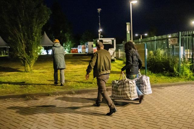 Nadia tilt de tassen van een man die noodgedwongen buiten moet blijven richting de plek waar ze een tentje wil opzetten voor hem. 