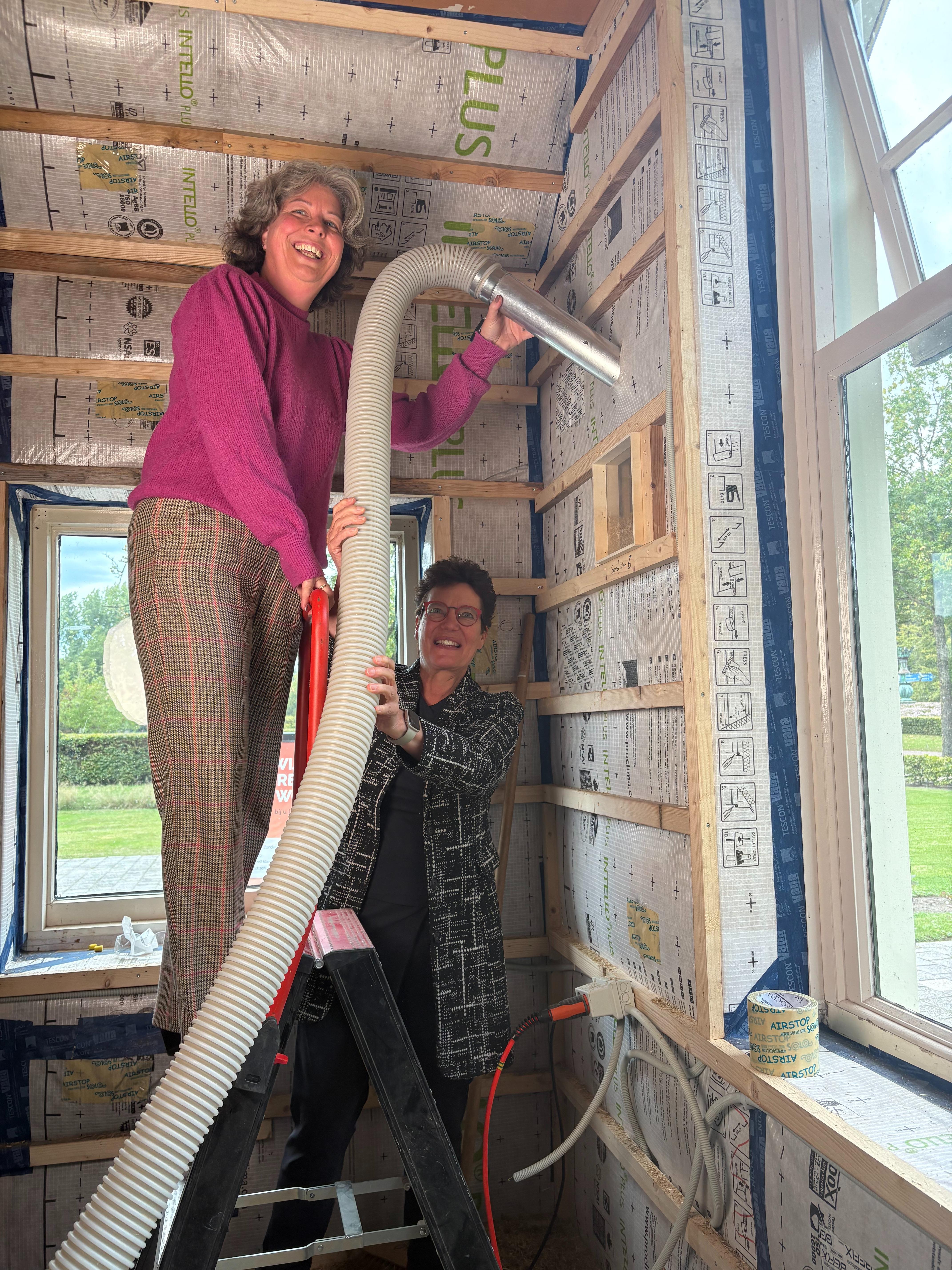 Gedeputeerde Yvonne Turenhout van de provincie Drenthe (onder) en wethouder Renate den Hollander van de gemeente Westerveld (boven) spuiten het gehakselde stro in de muur. 