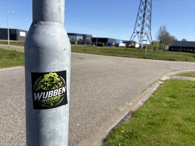 De sticker op een lantaarnpaal, met het bedrijf op de achtergrond.