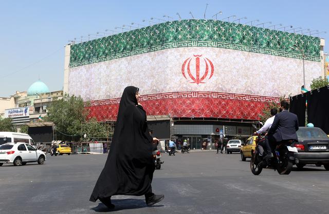 Een gesluierde Iraanse vrouw loopt langs een billboard met de nationale vlag van Iran op het Enqelab-plein in Teheran.