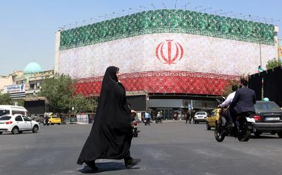 Een gesluierde Iraanse vrouw loopt langs een billboard met de nationale vlag van Iran op het Enqelab-plein in Teheran.