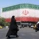 Een gesluierde Iraanse vrouw loopt langs een billboard met de nationale vlag van Iran op het Enqelab-plein in Teheran.