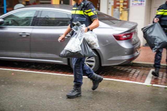 Een agent komt naar buiten met een tas vol wiet. Foto: Wesley Bos