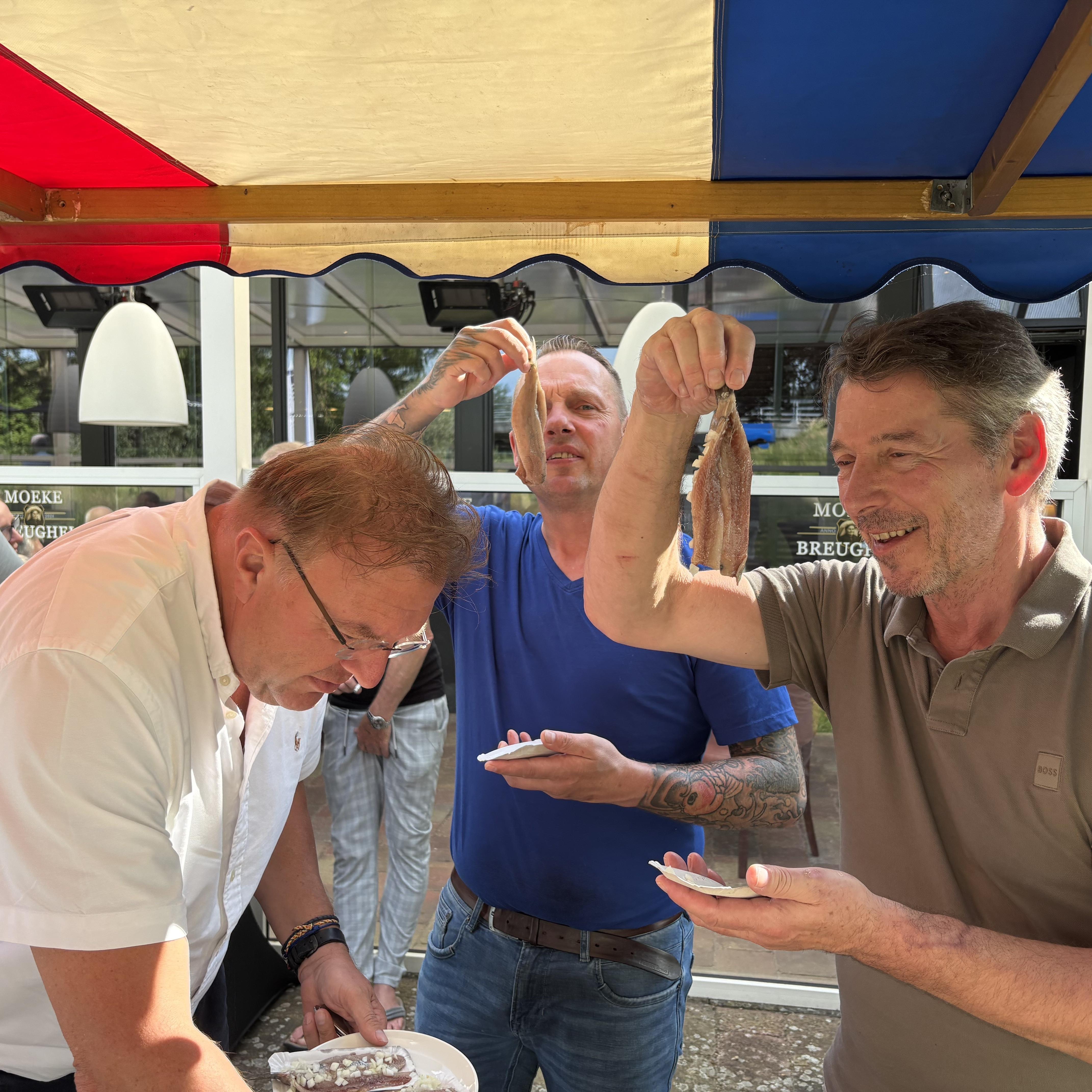 Wethouder Erich Wünker (links) serveert zichzelf een zoute haring. Vishandelaar Chris Lich (midden) en organisator Geert van Helden kijken verlekkert naar de haring.