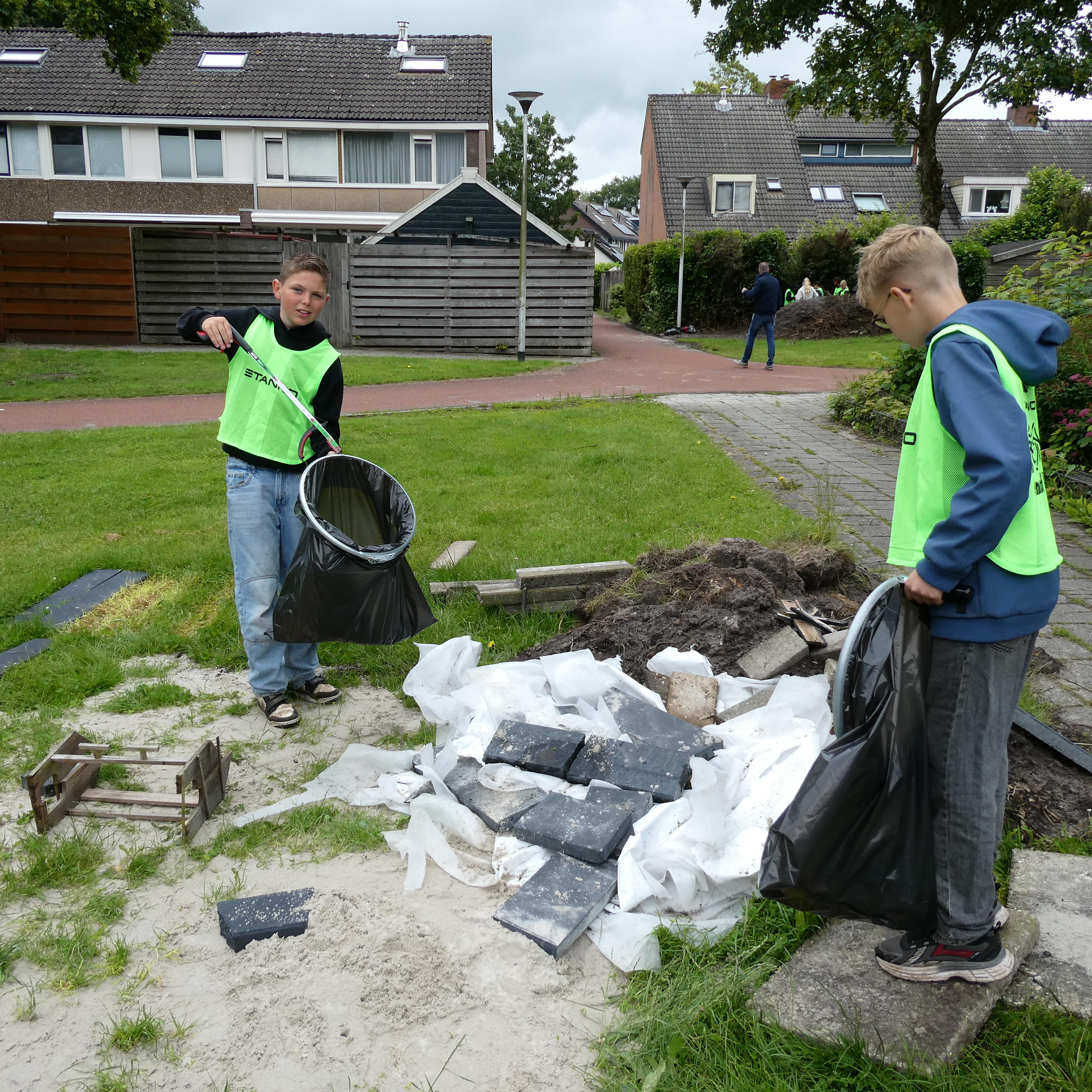 Twee leerlingen vullen vuilniszakken met zwerfafval en oud bouwpuin in de buurt rond de Hagenhofschool.