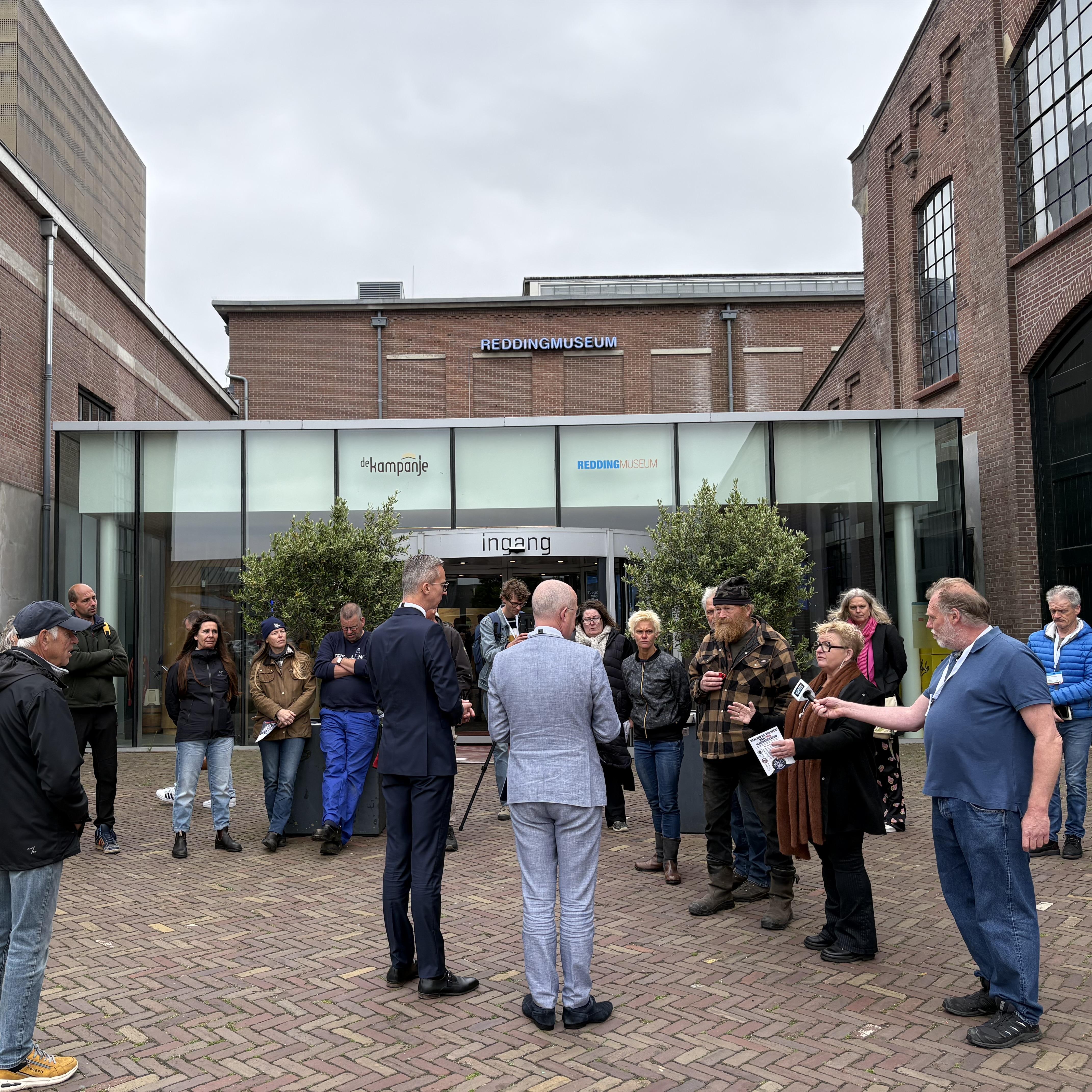 Hiltje Pootjes-Hofland (vierde van rechts) biedt Matthijs de Vries en Arno Brok in Den Helder een folder aan van Wij zijn de Wadden.